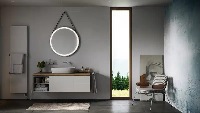 Modernes Badezimmer mit rundem LED-Spiegel, Waschplatz mit Aufsatzbecken, Handtuchheizkörper und minimalistischer Möblierung – concept 100 Serie im klaren Design.